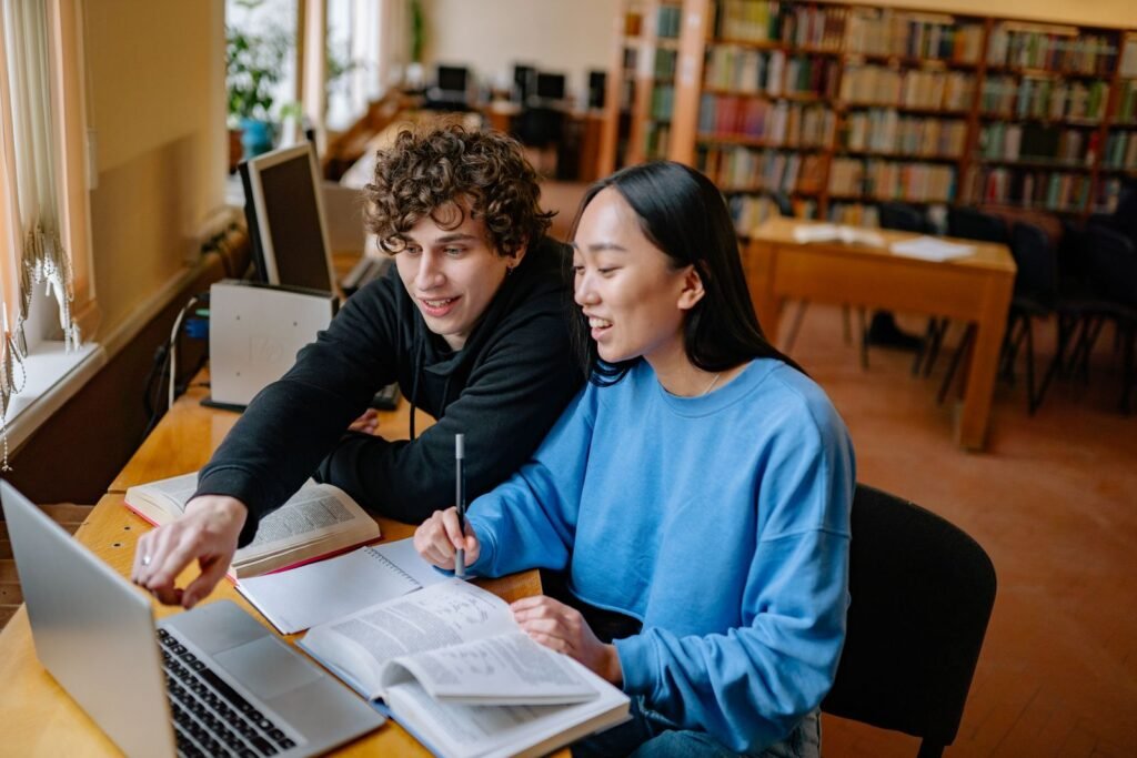 Students studying in a library with laptop and books